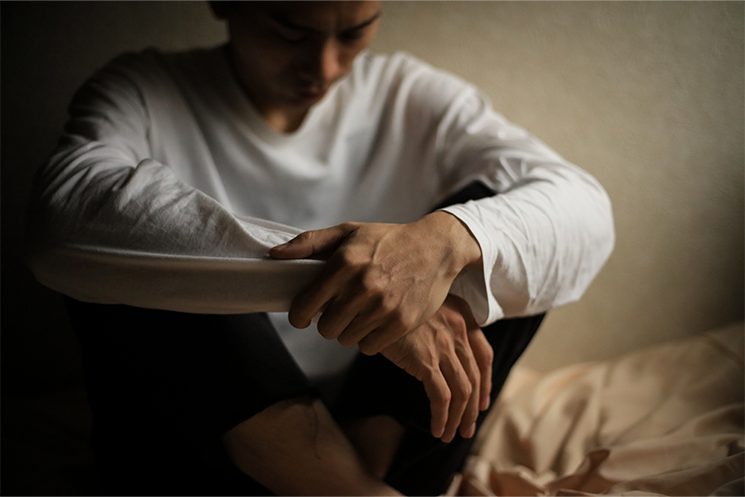 薄暗い部屋で頭を抱え葛藤する男性の姿。ADHD・ASDを抱えるWeb系プログラマのいぐぞー氏が指摘する、周囲から「言語化が足りない」という抽象的な指摘を受け、改善の処方箋が見つからずに努力の方向性を見失ってしまうエンジニアの心理的停滞状態を表現している。