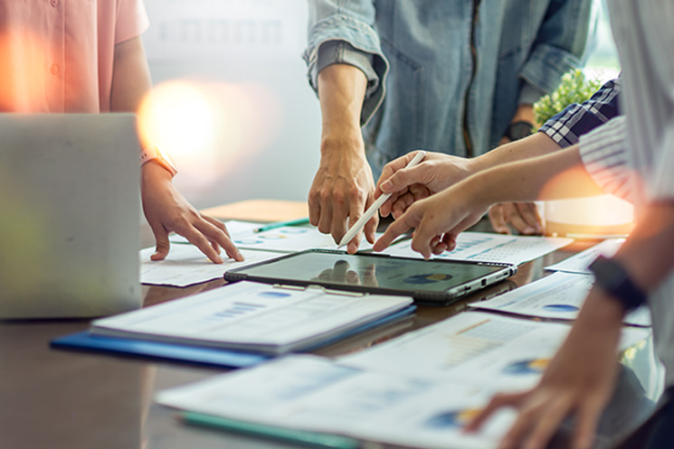 会議室でタブレットや資料を囲み議論するチームの風景。コードとは異なり、他人は自分の思い通りにコントロールできないというマネジメントの本質を表現している。強い言葉で相手を動かそうとする「逃避行動」の誘発ではなく、メンバーが自発的に動くマインドセットを醸成するための、コントロール不可能性の受容という文脈で使用