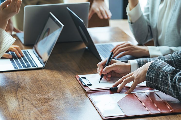 会議で資料を指し示し議論する様子。いぐぞー氏が提唱する「場面×行動×成果」でスキルを捉えるメソッド。要件定義なら「曖昧な要望の仕様化」、振り返りなら「事実と解釈の分離」など、抽象的な言語化力を具体的単位に分解することで、エンジニアが取り組むべき訓練を明確にする重要性を説いている。