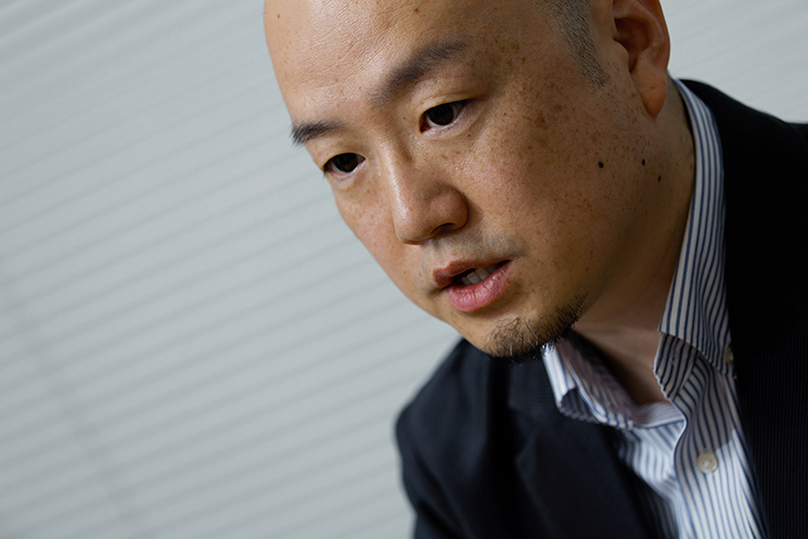 真剣な表情で諭すように語る間野健介氏。俳優が感情に溺れず、毎日同じシーンで涙を流すために「手順」を型として身につける経験を回想している。エンジニアもまた、実装への「没頭（没入）」とビジネス・ユーザー視点での「俯瞰（全体図）」という『二重の視点』を持ち、誰がいつ使っても価値を感じられる「再現性」の高いシステムを作るべきだと説く一場面。