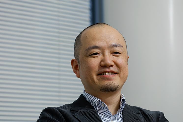 穏やかな笑みを浮かべる間野健介氏。「犯罪以外のことは何でも経験しろ」という俳優時代の師匠の言葉を引用し、画面の外で得たあらゆる失敗や成功の蓄積が、その人ならではの設計思想を形づくると語る。技術がコモディティ化する未来において、誰よりも深く人間を知ろうとする「血の通ったエンジニア」こそが最後に勝つという、レップ株式会社のビジョンを体現する結びの一場面。