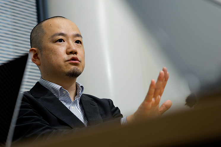 未来を見据えるような視線で語る間野健介氏。AIが導き出す「正解」としての効率的なコードを超え、顧客の期待を上回る「感動」を実装する重要性を説いている。仕様通りに作ったシステムが使われない悲劇を防ぐため、エンジニアの仕事を経験を形にする「表現」や「サービス」と捉え、対話を通じて相手の美意識やこだわりを設計に結びつける姿勢を示している。