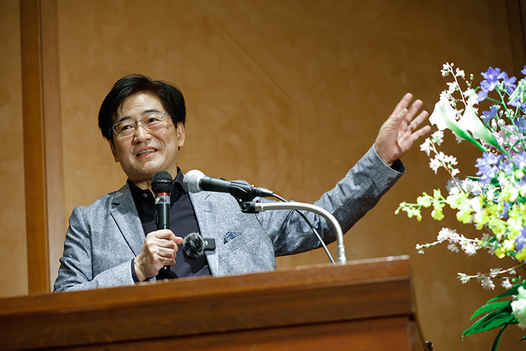 東京大学での最終講義を終え、清々しい表情で聴衆やスタッフへ謝辞を述べる暦本純一教授。「未来はすでにここにある。ただ、均等に行き渡っていないだけだ」という格言を引き、まだ一部にしかない未来の種を、誰にとっても自然で喜びを感じられる形へと社会実装していくことがこれからのエンジニアの本質的な仕事である、という力強いメッセージで講義を締めくくった