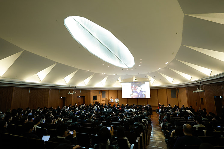 東京大学 伊藤謝恩ホールで開催された暦本純一教授の最終講義「不自然さを疑え」の会場俯瞰。18年半の教員生活の集大成を見届けるべく、会場を埋め尽くした多くのエンジニアや学生、研究者たちが、スクリーンに映し出された未来のインターフェースのビジョンを凝視している。AI時代の新たな指針が提示された歴史的な一日の熱気と会場の広がりを記録した一枚。