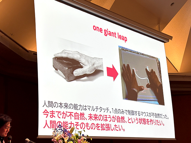 暦本純一教授の最終講義スライド。「one giant leap」という言葉と共に、ダグラス・エンゲルバートが発明した初期のマウスと、暦本氏が開発したマルチタッチ技術が対比されている。「1点のみで制御するマウスは不自然であり、複数の指を使うマルチタッチこそが人間の本来の能力を拡張する自然な未来である」という、従来の常識を疑う設計思想が説かれている場面。