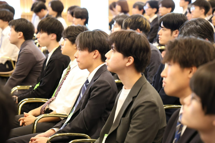 「第二回 AIチャレンジャーズフェス」にて、元デジタル大臣・河野太郎氏の講演を真剣な表情で聴講する若き学生エンジニアたち。AI翻訳や要約ツールが進化する激変期において、公式ドキュメント化される前の「未構造化の一次情報」や最先端のコミュニティへアクセスするために、生身の武器として英語を持つ生存戦略を学ぶ聴衆の様子。