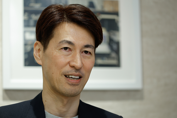 元DeNAのエンジニア・茂岩祐樹氏が、オークションサイト「ビッダーズ」時代に経験したエンジニアとしての原体験を回想する表情。受話器越しに聞こえたユーザーの赤ちゃんの泣き声から「自分たちのインフラが誰かの生活や商売を乗せている重み」を実感し、システムを死守する真の使命感に目覚めた瞬間を語る。