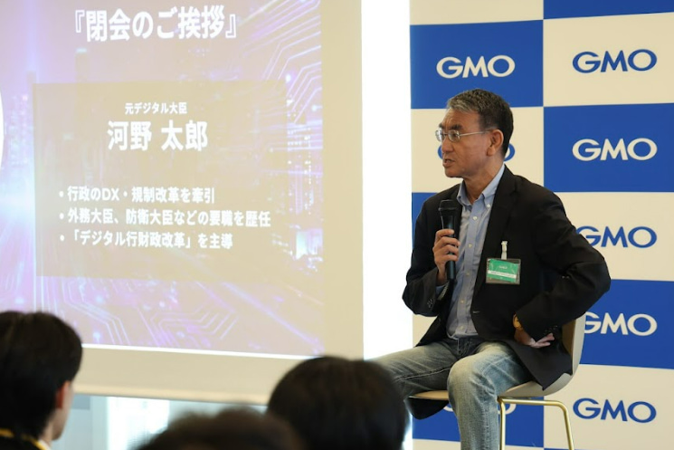 「第二回 AIチャレンジャーズフェス」の結びにて、外務大臣や防衛大臣などの要職を歴任した経歴スライドを背景に、世界で戦うための武器として「生身の英語」の必要性を訴える河野太郎氏。日本にいながら世界の最前線から知見を盗み出すための生存戦略を語り、若いAIエンジニアたちから第二、第三の大谷翔平や遠藤航が生まれることへの期待を寄せる場面。
