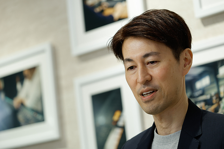 元DeNAインフラ統括・茂岩祐樹氏が、Mobage（モバゲー）急成長期にトラフィックが爆発し、ネットワーク帯域がパンクした「胃の痛い危機」を猛省とともに振り返るシーン。「常に1.5倍の余裕を持つ」という経営陣との約束、過信によるバッファー確保の遅れ、そして数ヶ月待ちの回線増設を待たずに全社でHTMLを削り出すアナログな力技へ移行したエンジニアリングの教訓。