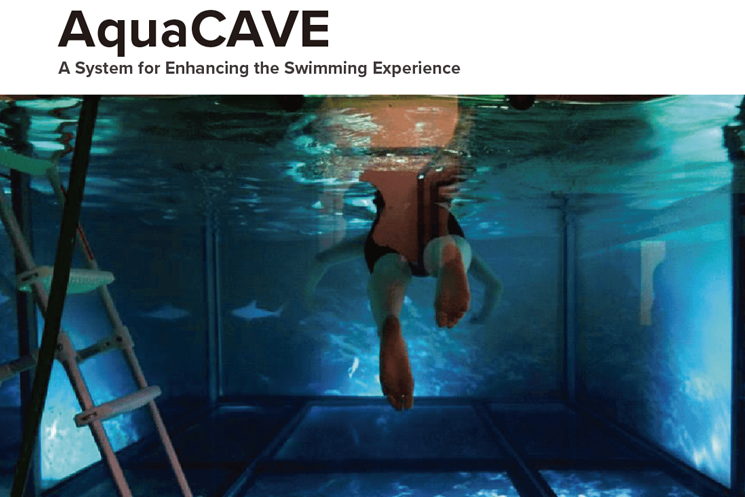 暦本研究室が開発した水上・水中没入型VRシステム「AquaCAVE」の実験風景。プール水槽の壁面スクリーンにサンゴ礁や海の立体映像が投影され、液晶シャッター付き水中メガネを装着した泳者が、赤外線カメラによる頭部追跡と連動した臨場感ある映像空間の中を泳いでいる様子（出典：暦本研究室 研究集録 2007-2026）