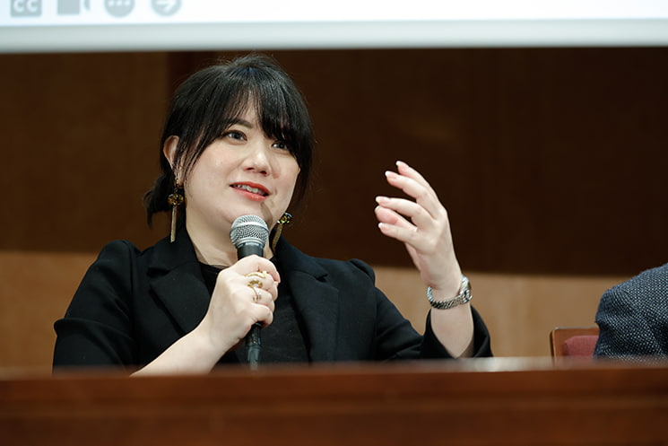 暦本純一教授の最終講義にて、教授が未来を提示することで世界のテクノロジー進化が早まっている事実を「遺伝的アルゴリズム」の言葉で表現し、50年先、100年先の未来を見せてくれた感謝とともに、退官後もカオスな状態で進化を促進させてほしいという願いを、左手を掲げ敬意を込めた眼差しで語る玉城絵美氏