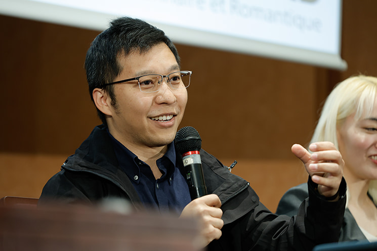 暦本純一教授の最終講義にて、入試直後に「プール（AquaCAVE）でプログラムを動かして」といきなり課題を出され毎日焦っていた過去を振り返りながら、そこから「ゴールから逆算して必要な知識を身につければいい」と発想を転換したエピソードをマイクを手に笑顔で語る、Huaweiで最先端ラボを率いる張鑫磊氏
