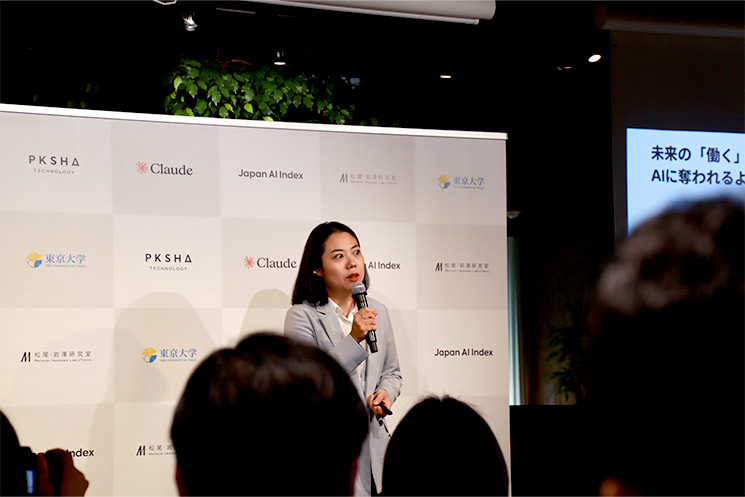 2026年6月の「Japan AI Index」発表会にてマイクを握り登壇するPKSHA Technology CEO室室長の大野紗和子氏。日本企業独自のボトムアップ型カイゼン文化や低い雇用流動性が、社内システムやソースコードの個別化・暗黙知化を生み、英語圏のオープンソースを学習した汎用AIでは対応できないレガシー環境の現場コンフリクトを引き起こす背景を指摘している