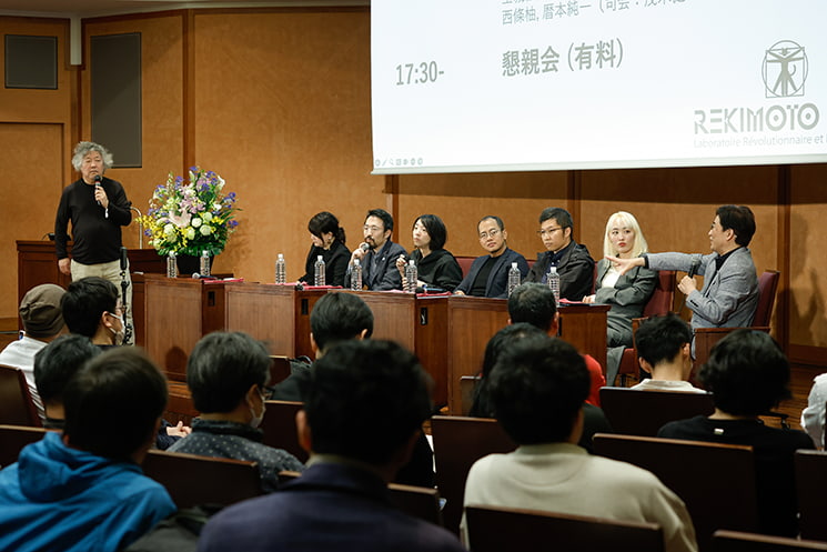 東京大学の伊藤謝恩ホールにて、多くのオーディエンスで埋め尽くされた客席の後方から、ステージ上で「スマートスキン（SmartSkin）」開発時のアマチュア精神やAI時代のキャリアモデルを熱弁する暦本純一教授、並び立つ卒業生パネリスト、司会の茂木健一郎氏の姿を一望する会場全体の風景