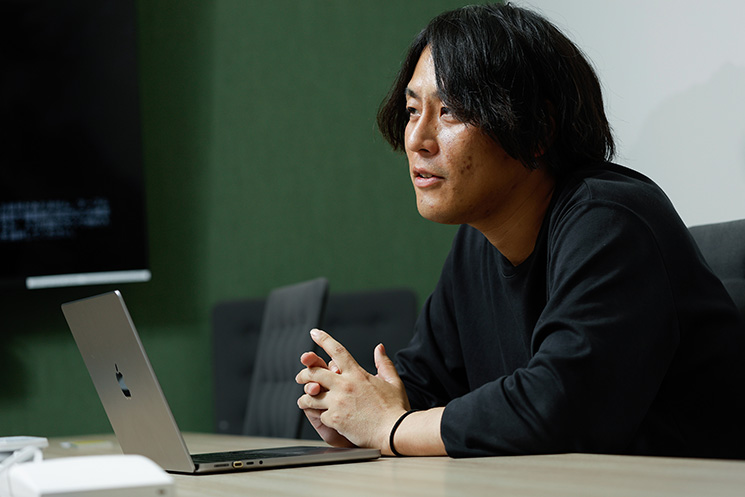 年々増加するソフトウエア脆弱性と優先順位付けの課題について語る、株式会社grasysの吉田悠介さん。ノートPCを開き、手を組んでインタビューに応える姿