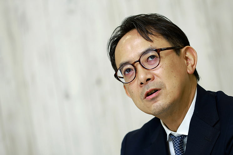眼鏡をかけた前LINEヤフー代表取締役会長の川邊健太郎氏が、思考を巡らせるような強い視線で上を見つめる接写ポートレート。30年間のネット企業経営を通じて「組織やエンジニアのマネジメントが不可欠だった時代」を振り返り、AIやバイブコーディングの登場によって個人が直接プロダクトを作れる時代へと変化した構造的ギャップを語る場面に配置されている