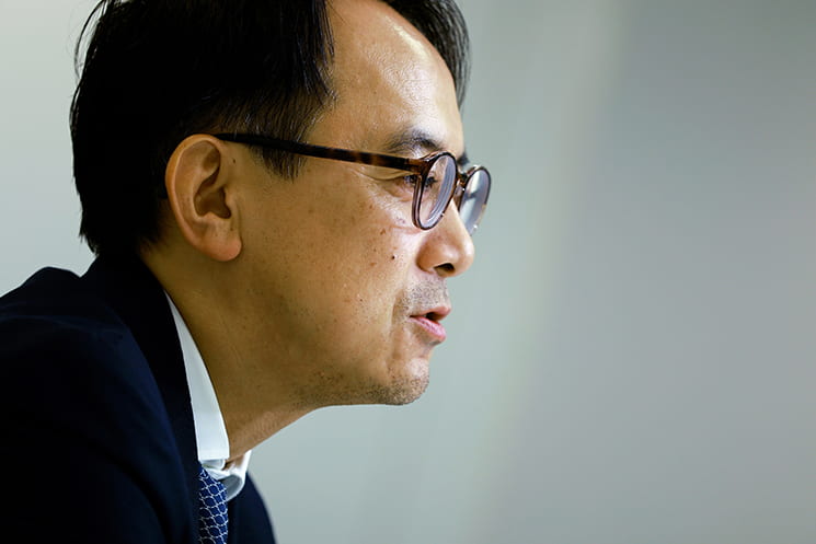 眼鏡をかけた前LINEヤフー代表取締役会長の川邊健太郎氏が、横顔で真剣に訴えかけるポートレート。感性だけに頼るのではなく、まずは自身でバイブコーディングを行い実際に使えるソフトウェアを作る体験をしなければAIの真の可能性や自分の「やりたいこと」は見えてこないと、AI活用の核心を強調する場面に配置されている