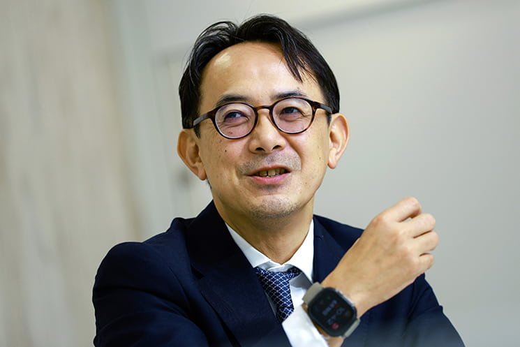 眼鏡をかけた前LINEヤフー代表取締役会長の川邊健太郎氏が、親しみやすい笑顔で斜め上を向くポートレート。記事本文では、AI時代に重要な「やりたいこと」の見つけ方として、自身のWikipediaでの経験を例に、ハイパーリンク構造を通じて無制限に広がる人間の好奇心と意思の重要性を語る場面に配置されている