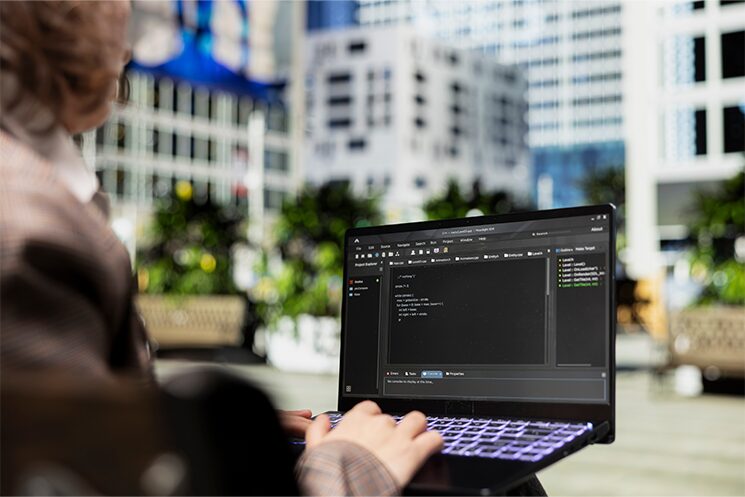 屋外でノートPCを開き、プログラミングをするエンジニア。組織に属して「仕事のための仕事」に時間を割くことへのストレスから、エンジニアとしての仕事に集中できる自由な働き方を求め、フリーランスを選ぶ人が増えてきた背景を示す